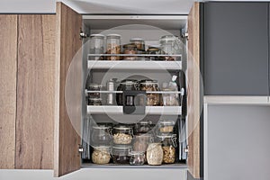 Variety of dry foods, grains, nuts, cereals in glass jars in kitchen cupboard.