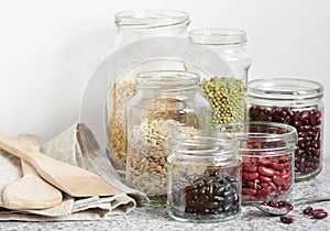 Variety of dry legumes: kidney bean, peas, green gram in glass jars uncooked on white kitchen background