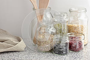 Variety of dry legumes: kidney bean, peas, green gram in glass jars uncooked on white kitchen background