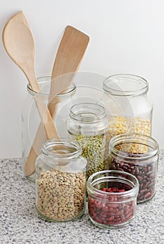 Variety of dry legumes: kidney bean, peas, green gram in glass jars uncooked on white kitchen background, zero waste, eco friendly