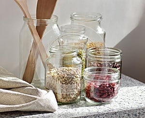 Variety of dry legumes: kidney bean, peas, green gram in glass jars uncooked on white kitchen background, zero waste, eco friendly