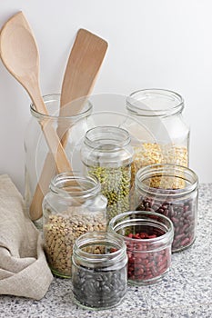 Variety of dry legumes: kidney bean, peas, green gram in glass jars uncooked on white kitchen background, zero waste, eco friendly