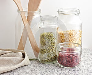 Variety of dry legumes: kidney bean, peas, green gram in glass jars uncooked on white kitchen background, zero waste, eco friendly