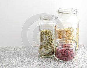 Variety of dry legumes: kidney bean, peas, green gram in glass jars uncooked on white kitchen background, zero waste, eco friendly