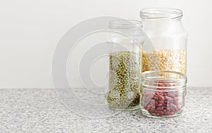 Variety of dry legumes: kidney bean, peas, green gram in glass jars uncooked on white kitchen background, zero waste, eco friendly