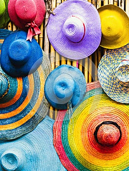 Variety of fashionable and colorful hats hanging on bamboo backdrop of curbside shop. Tourism designer straw hats from the sun of