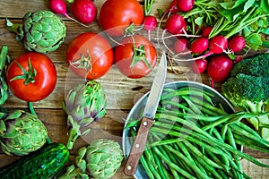 Variety of fresh colorful organic vegetables green beans, tomatoes, red radish, artichokes, cucumbers on wood kitchen table, copy