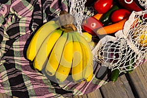 Variety of fresh organic fruits and vegetables in avoska on the tablecloth. Banana, carrot, tomato in string bag. Healthy eating