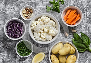 Variety of fresh vegetables in bowls - potatoes, red and cauliflower, spinach, green onions, carrots, nuts, olive oil, cilantro.