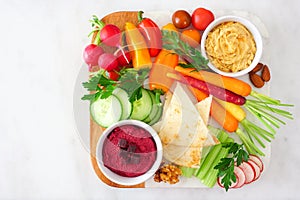 Variety of fresh vegetables and hummus dip on a platter, top view on white marble