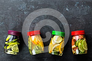 Variety of fruit infused detox water in jars for a healthy diet top view on a dark background