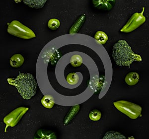 Variety of green vegetables on black table as broccoli, peppers, tomatoes and cucumbers