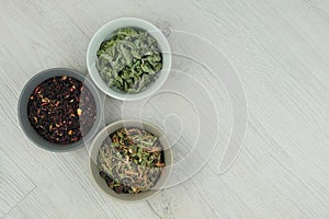 Variety of herbal teas in bowls on a light wooden background. Set of aromatic leaves. Top view.