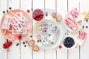 Variety of homemade berry yogurt popsicles, top view table scene over white wood