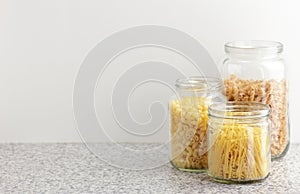 Variety of italian pasta in glass jars uncooked on white kitchen background