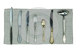 Variety of knives, forks and other kitchen utensils on a linen napkin isolated on a white background. Top view.