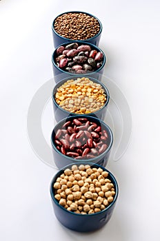 A variety of legumes. Lentils, chickpeas, peas and beans in blue bowls on a white background. Close-up