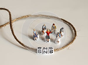 A variety of miniature people sitting with  `SNS` alphabetical white cube.