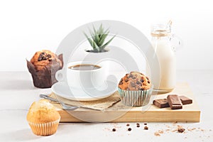A variety of muffins with a cup of milk chocolate on a wooden board on a white background