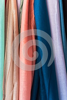 Variety of multicolored fine organic cotton scarves of pastel colors hanging at store display market. Elegant feminine style