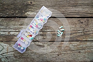 Variety of pills in white plastic pill organizer on weathered wood