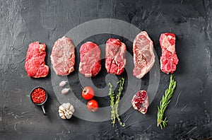 Variety of raw alternative steaks picanha, ramp and chuck eye roll and top blade with herbs for grill over black background top