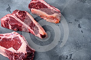 Variety of Raw Black Angus Prime Dry aged meat steaks, tomahawk, t bone or porterhouse and club steak, on gray stone background,