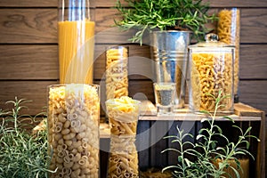 Variety of raw dry pasta penne,fusilli,macaroni,spaghetti,shapes of pasta in glass jars on a wooden table,set or many different