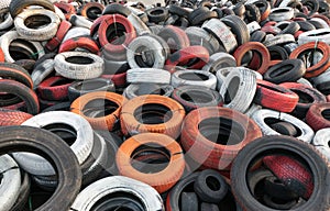 Variety of red white orange and black waste car tires piled in a big pile