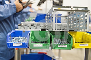 Variety of screws in tray with engineers working at electronics industry