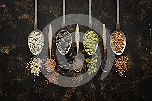 A variety of seeds in spoons, chia, flax, pumpkin, sunflower, coriander, sesame, black sesame on a dark background. Top view, copy