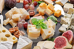 Variety of sliced cheeses with fruits, mint, nuts and cheese cutting knives
