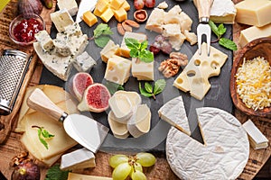 Variety of sliced cheeses with fruits, mint, nuts and cheese cutting knives