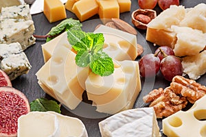 Variety of sliced cheeses with fruits, mint, nuts and cheese cutting knives