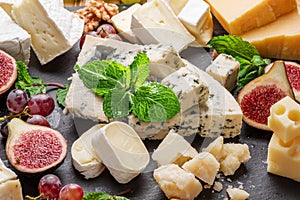 Variety of sliced cheeses with fruits, mint, nuts and cheese cutting knives.