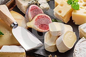Variety of sliced cheeses with fruits, mint, nuts and cheese cutting knives. photo