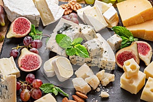 Variety of sliced cheeses with fruits, mint, nuts and cheese cutting knives photo