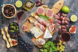 A variety of snacks, prosciutto,grapes, wine, cheese with mold, figs, basil, olives on a rustic background. Top view,flat lay