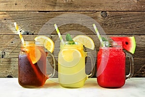 Iced tea, lemonade and watermelon juice summer drinks in mason jar glasses against dark wood photo