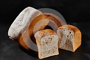 Variety of tasty baked bread, whole and cut in halves, sprinkled with flour. Black background, copy space. Close-up