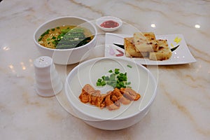 A variety of traditional dim sum dishes on dining table in restaurant. Porridge, and egg noodles in bowls, and pan fried turnip