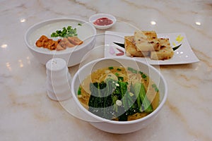A variety of traditional dim sum dishes on dining table in restaurant. Porridge, and egg noodles in bowls, and pan fried turnip