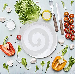 Variety of vegetables laid out around a white plate with oilknife and fork wooden rustic background top view close up