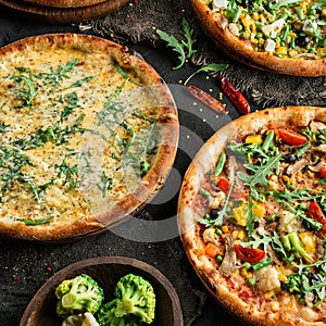 Variety of vegetarian pizzas with cheese, greens, vegetables on wooden board over black background. Fast food lunch, gathering,