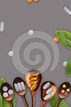 Variety of vitamin pills in wooden spoon on gray background with green leaf.