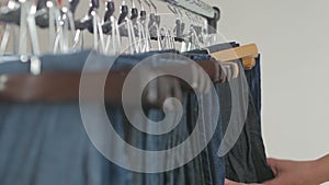 A variety of women`s denim pants hanging on a hanger. Woman chooses her clothes in the store. Hands close up