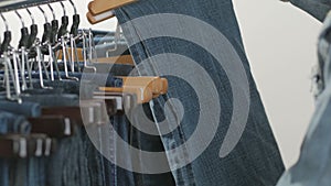 A variety of women`s denim pants hanging on a hanger. Woman chooses her clothes in the store. Hands close up