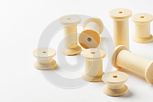 Variety of wooden thread spools reels of different sizes scattered on white background. Sewing crafts hobbies tailoring fashion