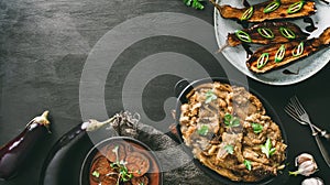 Various baked eggplant dishes, grilled eggplant with spicy sauce, mashed eggplant with parsley on pan, black wooden background,