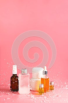 Various bottles, jars and containers with cosmetics on pink with splashing waters.